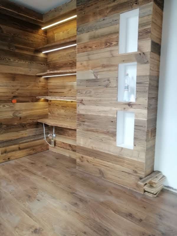 Drewniana zabudowa wnętrza z półkami podświetlonymi LED i wnękami w ścianie. Podłoga z paneli imitujących drewno. Wykończenie w rustykalnym stylu.
