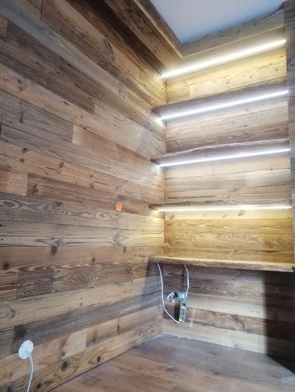 Drewniana boazeria z podświetlanymi półkami wnękowymi, widoczne kable. Realizacja w Żmigrodzie. Ciepłe oświetlenie podkreśla naturalny rysunek drewna.