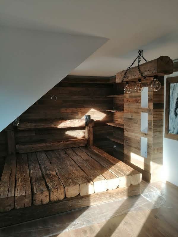 Drewniana zabudowa wnętrza z surowych bali: ściana, półki i podest. Oświetlenie z żarówek na łańcuchu. Naturalne drewno, minimalistyczny design, jasne wnętrze.