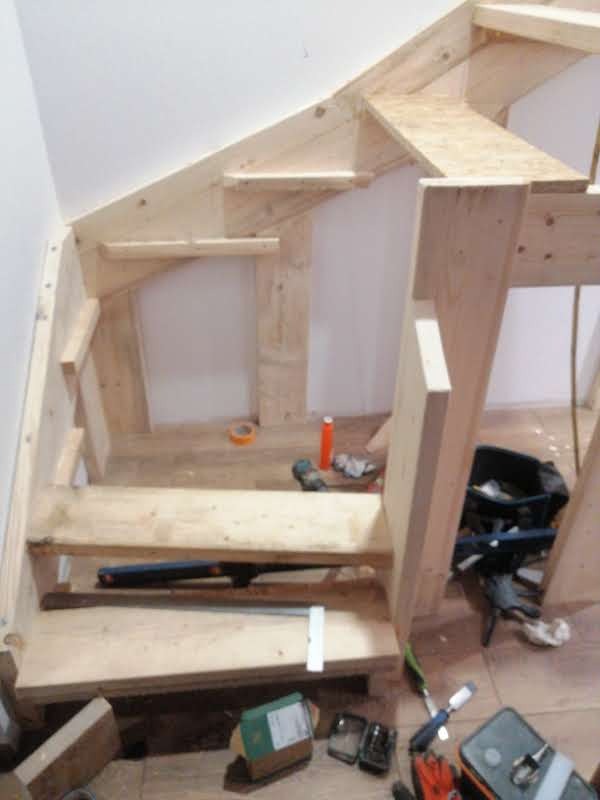 Szkielet drewnianej konstrukcji schodów poddaszowych w trakcie budowy, z narzędziami i akcesoriami stolarskimi w tle.