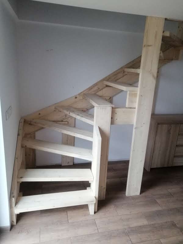 Surowe, drewniane schody wewnętrzne, jeszcze nie wykończone, z widoczną konstrukcją.  Podłoga z paneli imitujących drewno. Ściany pomalowane na jasny kolor.