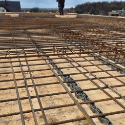 MAR-BUD Marcin Świerkosz - Zbrojenie płyty fundamentowej z widocznymi dystansami z tworzywa sztucznego i sylwetką pracownika w oddali.