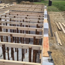 MAR-BUD Marcin Świerkosz - Wznoszenie ścian z bloczków betonowych, widoczne drewniane podpory i szalunki, przygotowanie do dalszych prac budowlanych.