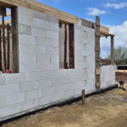 MAR-BUD Marcin Świerkosz - Wznoszenie ścian domu z betonu komórkowego, widoczne drewniane szalunki i podpory, w tle błękitne niebo z chmurami.