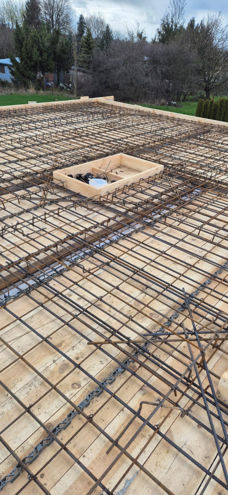 Zbrojenie płyty fundamentowej ułożone na deskowaniu, widoczny otwór na instalacje i plastikowe dystanse pod zbrojeniem.