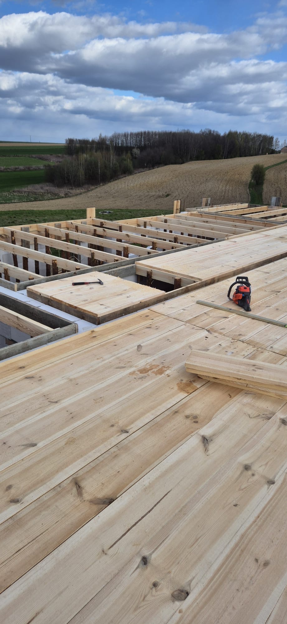 Wiązanie drewnianego stropu na fundamencie domu jednorodzinnego, widoczna piła spalinowa i młotek.