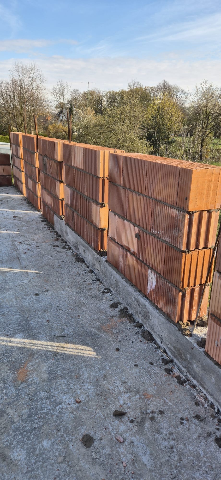 Wznoszenie ścian z czerwonej ceramiki w Wielopolu Skrzyńskim, widoczne zbrojenie pionowe, fundament z betonu.