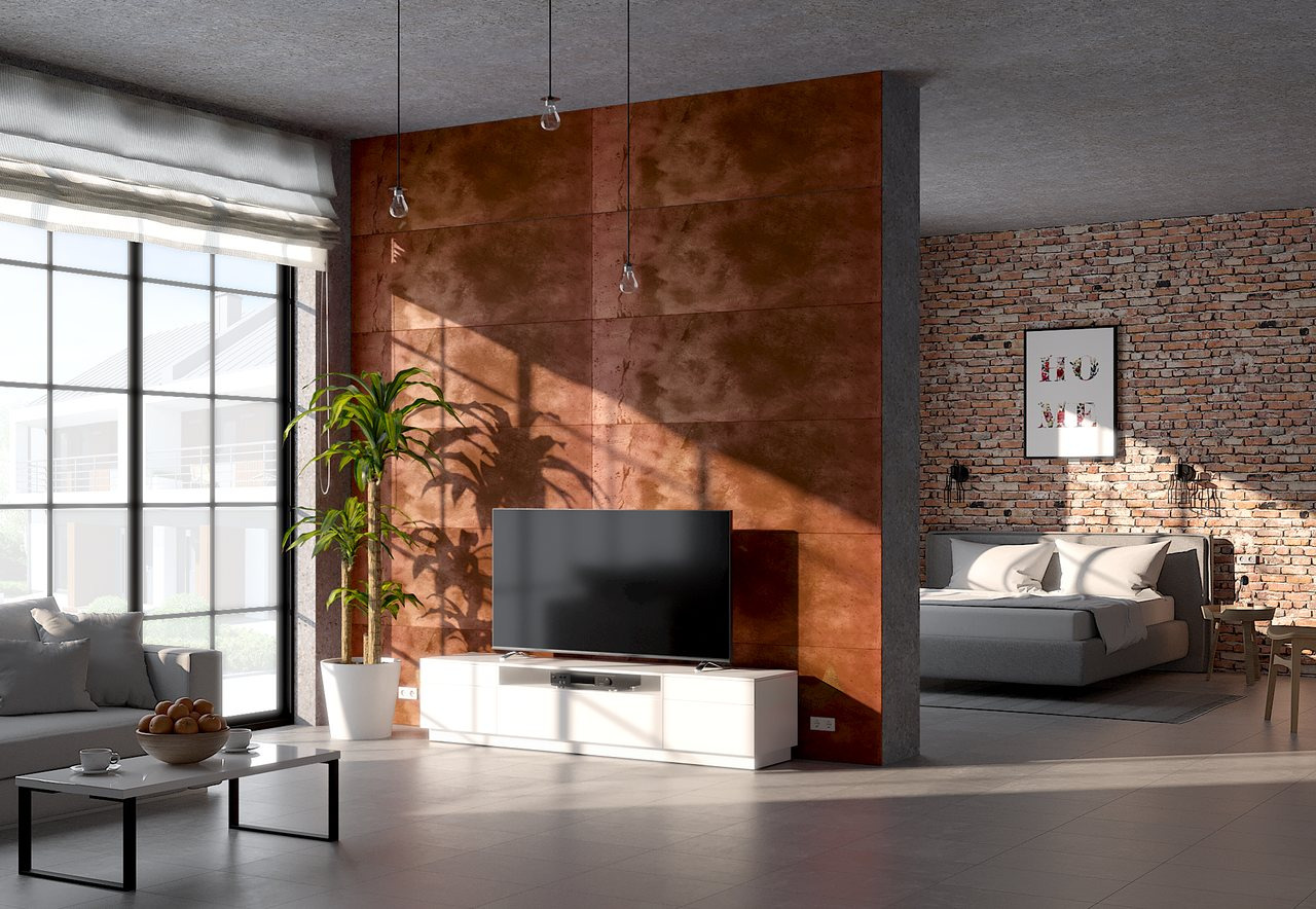 Nowoczesny salon z dekoracyjną ścianą z paneli w kolorze rdzawym, dzielącą przestrzeń na część dzienną i sypialnię z ceglaną ścianą, oświetlony popołudniowym słońcem wpadającym przez duże okno.
