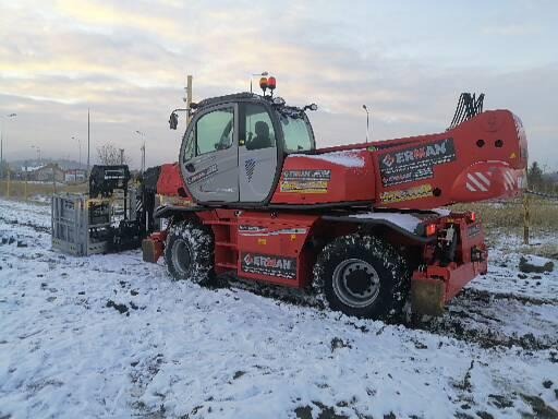 Czerwony wózek widłowy teleskopowy marki ERMAN stoi na zasypanym śniegiem terenie budowy przy pochmurnym niebie.