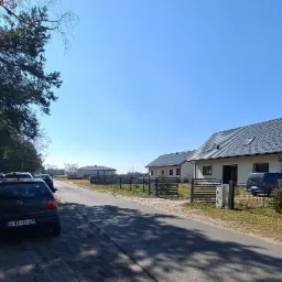 Nowoczesne domy jednorodzinne z szarą dachówką i ogrodzeniem panelowym w słoneczny dzień, samochody zaparkowane wzdłuż drogi.