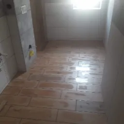 Wykończona łazienka z podłogą z płytek imitujących drewno, szare płytki na ścianach częściowo wykończone, widoczny odpływ liniowy i instalacja podtynkowa WC.