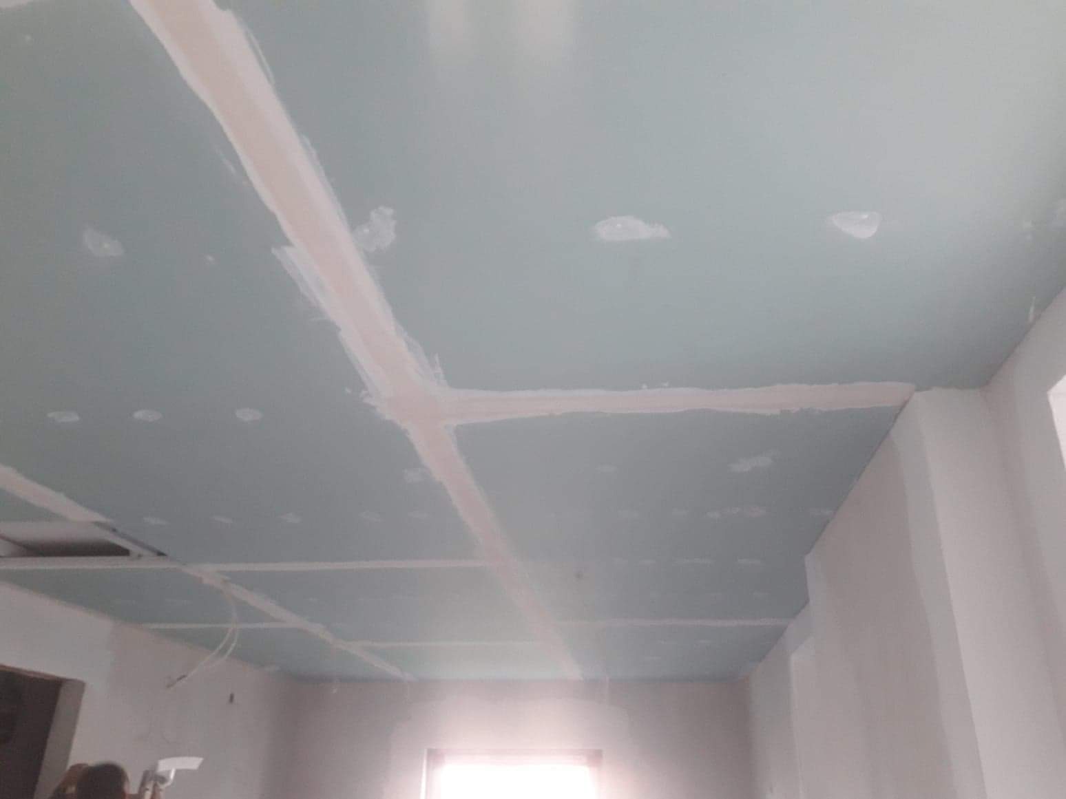 Montaż sufitu z płyt kartonowo-gipsowych, widoczne łączenia płyt wypełnione masą szpachlową, przygotowane do dalszej obróbki.