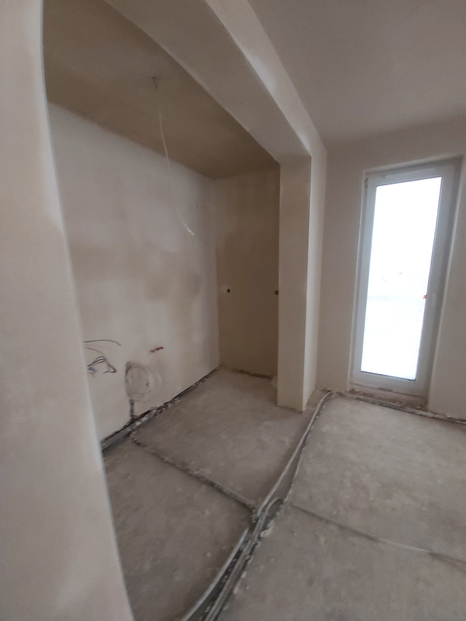 Wnętrze w stanie deweloperskim z widocznymi przewodami elektrycznymi i instalacją podłogową przed wylewką, ściany przygotowane pod tynkowanie.