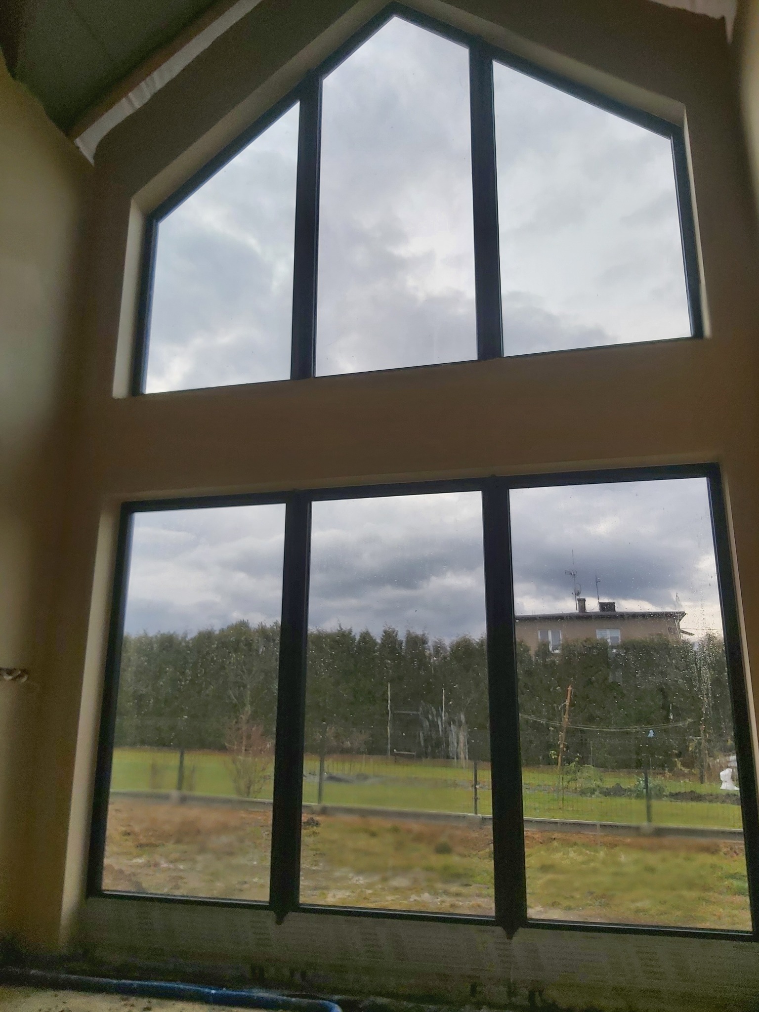 Surowy stan ścian wewnętrznych z dużymi oknami, widoczne niedoskonałości tynku i przygotowanie do dalszych prac wykończeniowych.