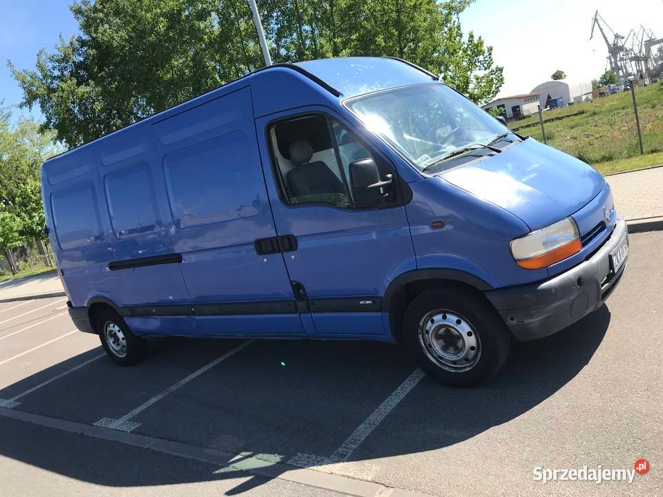 Niebieski samochód dostawczy Renault Master zaparkowany na parkingu, widoczne ślady użytkowania na karoserii, w tle żurawie portowe.