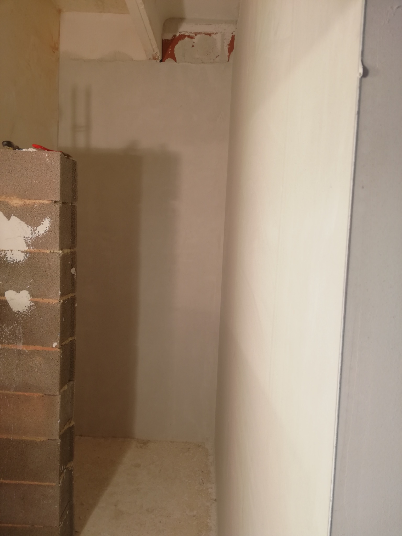 Wnętrze w trakcie prac przygotowawczych: otynkowana ściana, fragment muru z pustaków z resztkami zaprawy, surowy beton na podłodze.