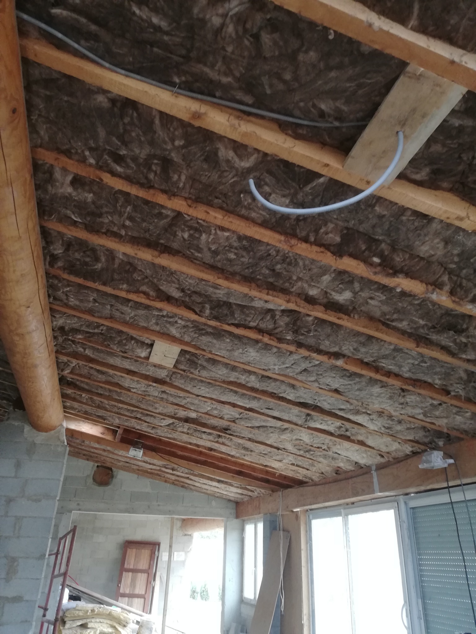 Poddasze z drewnianą konstrukcją, ocieplone wełną mineralną, widoczne przewody elektryczne i fragment ściany z pustaków.