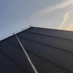 Metalowy dach z zamontowaną instalacją odgromową, widoczne przewody i zwody pionowe na tle błękitnego nieba i drzew