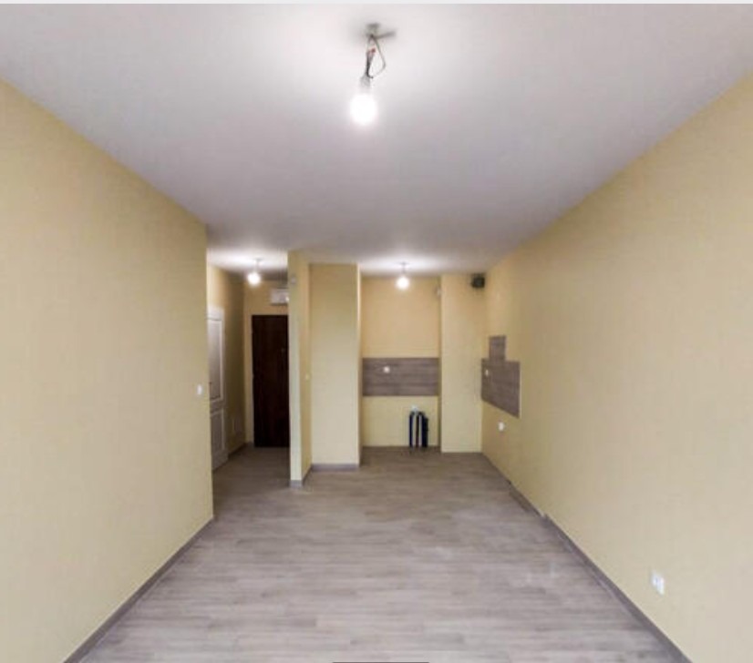 Wnętrze mieszkania po malowaniu ścian na jasny odcień beżu, widoczne fragmenty przygotowane pod płytki w kuchni, surowa żarówka zwisająca z sufitu.