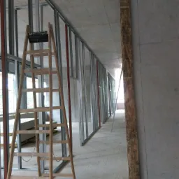 Wnętrze w trakcie montażu ścian działowych z profili stalowych, widoczna drewniana drabina i płyty gipsowo-kartonowe.