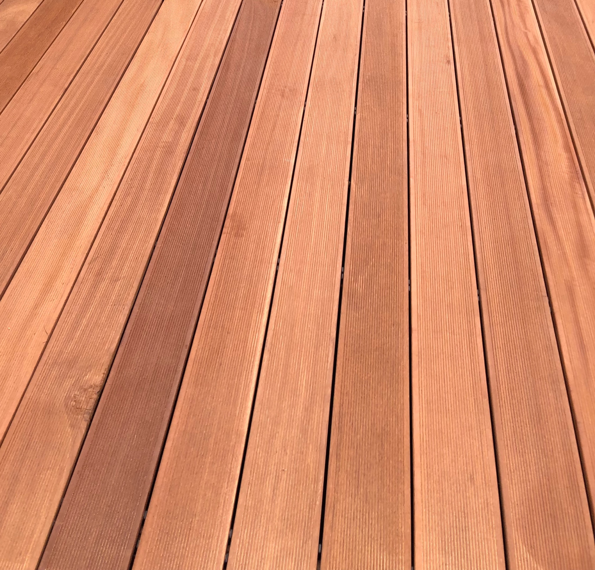 Ukończony taras z desek kompozytowych w odcieniach brązu, ułożonych równolegle. Widoczna faktura drewna i regularne odstępy między deskami.