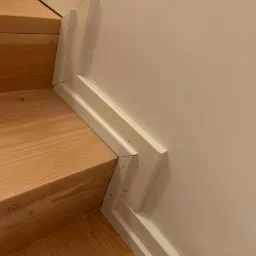 Detail of a staircase showing the finished baseboard trim where the stairs meet the wall, secured with visible nail holes.