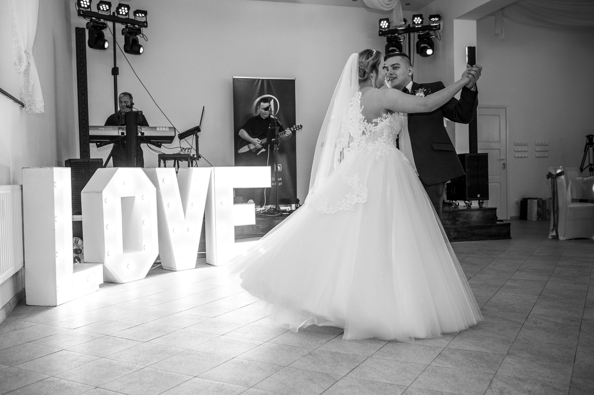 Para młoda w pierwszym tańcu, z zespołem muzycznym w tle i dekoracją LOVE z podświetlanych liter.