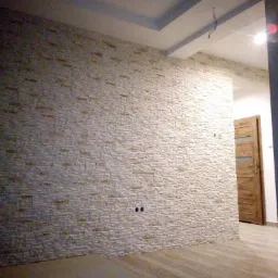 Ściana wykończona dekoracyjną okładziną imitującą kamień, z widocznymi puszkami elektrycznymi, drewniana podłoga i drzwi w tle, sufit z elementami dekoracyjnymi.