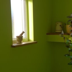 LECH-POL Leszek Duks Usługi Ogólnobudowlane - Świeżo pomalowane na limonkowo wnętrze łazienki z oknem, na parapecie moździerz z pistlem, półka z dekoracyjnymi wazonami i zielona toaleta w rogu.