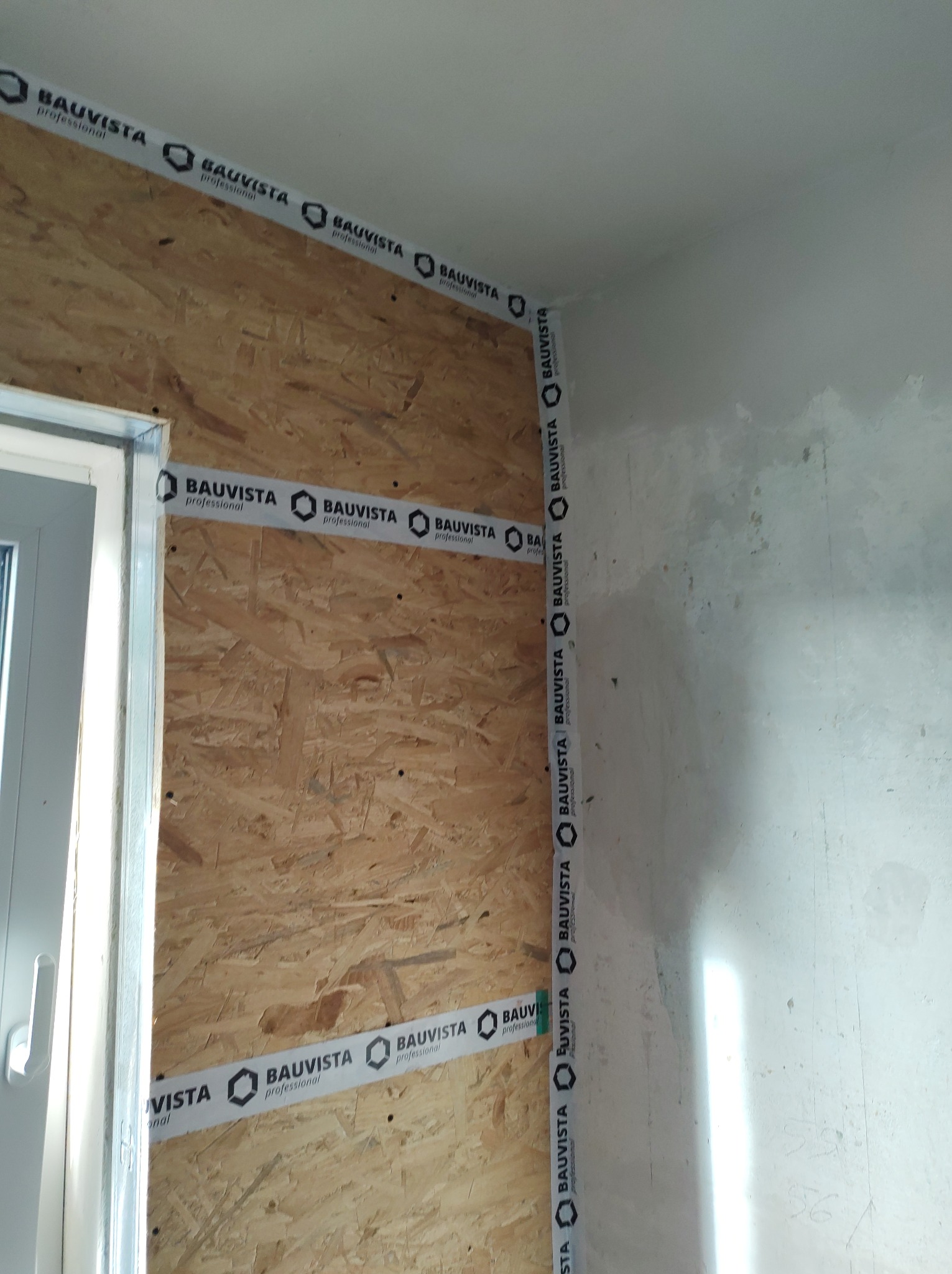 Przygotowanie ściany z płyty OSB do dalszych prac wykończeniowych, zabezpieczona taśmą Bauvista Professional, widoczne surowe wykończenie ściany obok okna.
