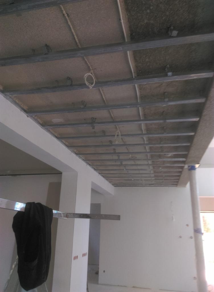 Stelaż sufitowy z profili metalowych i częściowo zamontowanych płyt w pomieszczeniu w trakcie remontu, widoczne kable i elementy mocujące.