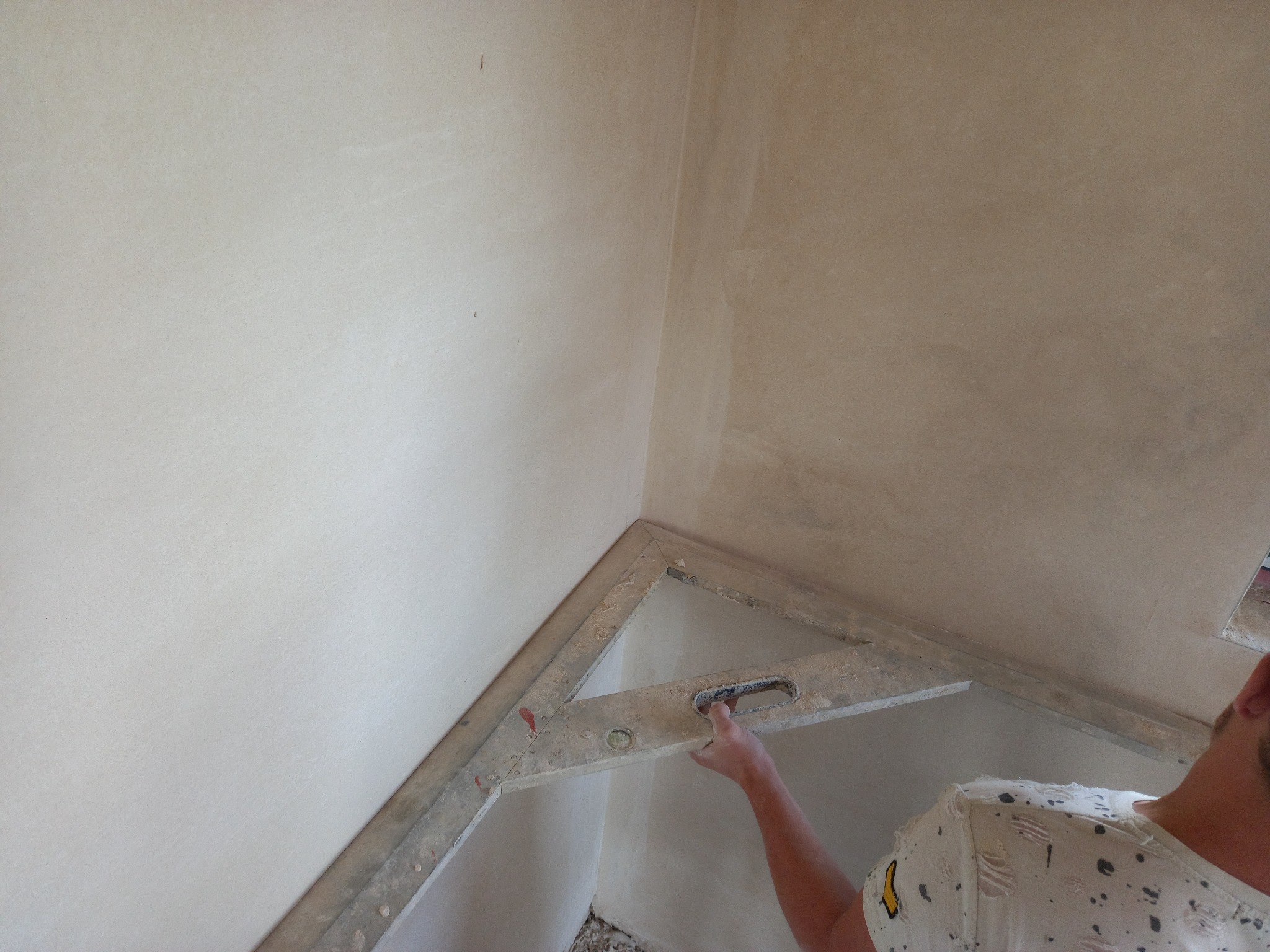 Sprawdzanie pionu świeżo nałożonego tynku na ścianie przy użyciu poziomicy, widoczne drobne niedoskonałości powierzchni.