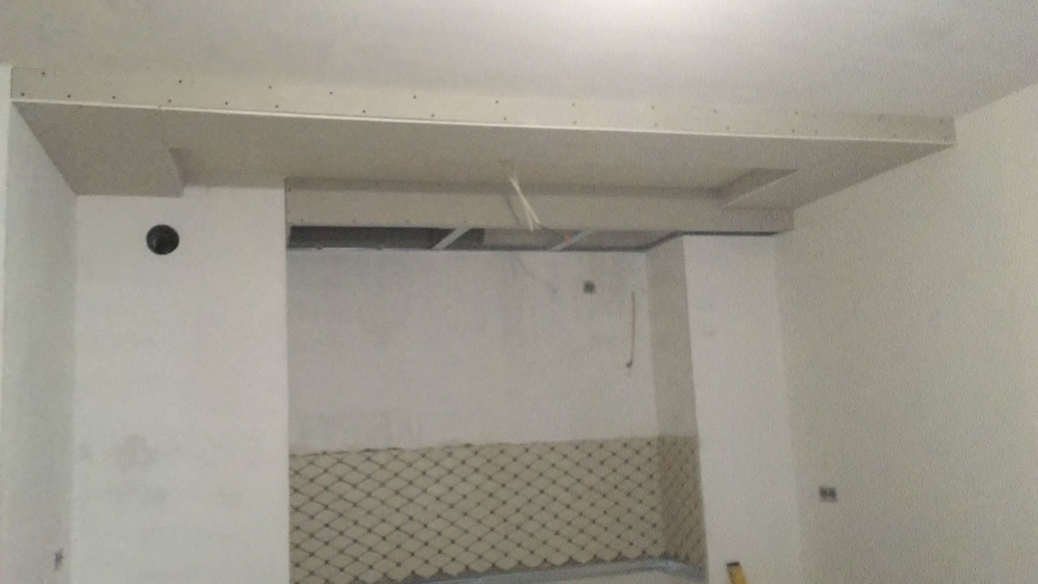 Wnętrze w trakcie prac wykończeniowych: częściowo obłożona płytkami ściana, zamontowany stelaż sufitu podwieszanego z płyt gipsowo-kartonowych, widoczne przewody elektryczne.