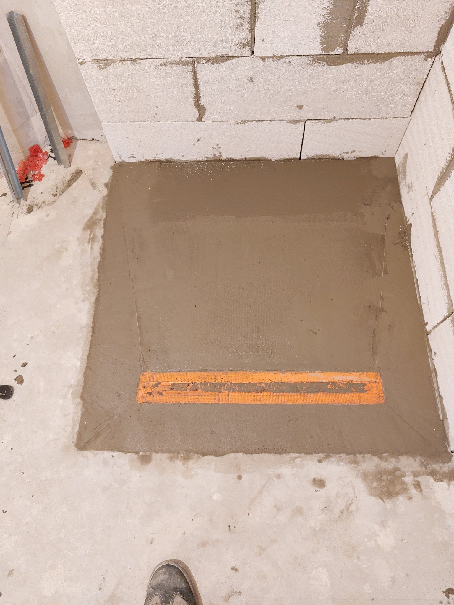 Przygotowanie podłoża pod prysznic: wylewka betonowa z zamontowanym odpływem liniowym, ściany z bloczków betonowych, widoczne elementy instalacyjne.