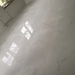 Jasne, błyszczące płytki podłogowe imitujące marmur w nowym wnętrzu w Słubicach, z widocznym oknem i grzejnikiem na ścianie.