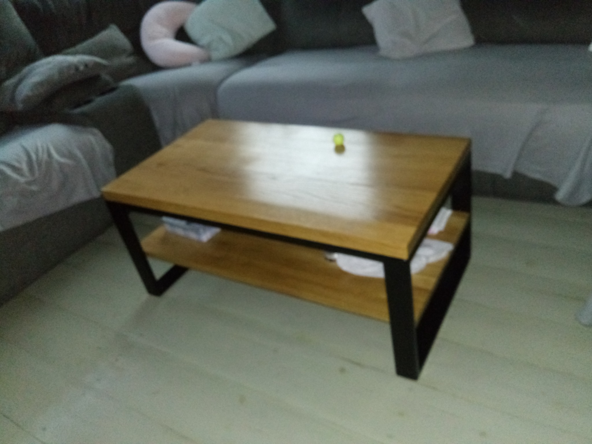 Stolik kawowy z drewnianym blatem i metalową ramą w salonie, na blacie leży mała piłeczka.