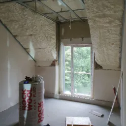 Poddasze w trakcie ocieplania pianką PUR, widoczna konstrukcja sufitu podwieszanego, okno, oraz rolka wełny mineralnej Rockwool.