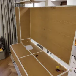 Montaż korpusu meblowego z drewnopodobną okleiną w Radomiu, widoczne zabawki na blacie i kartka papieru, sugerujące etap prac wykończeniowych.