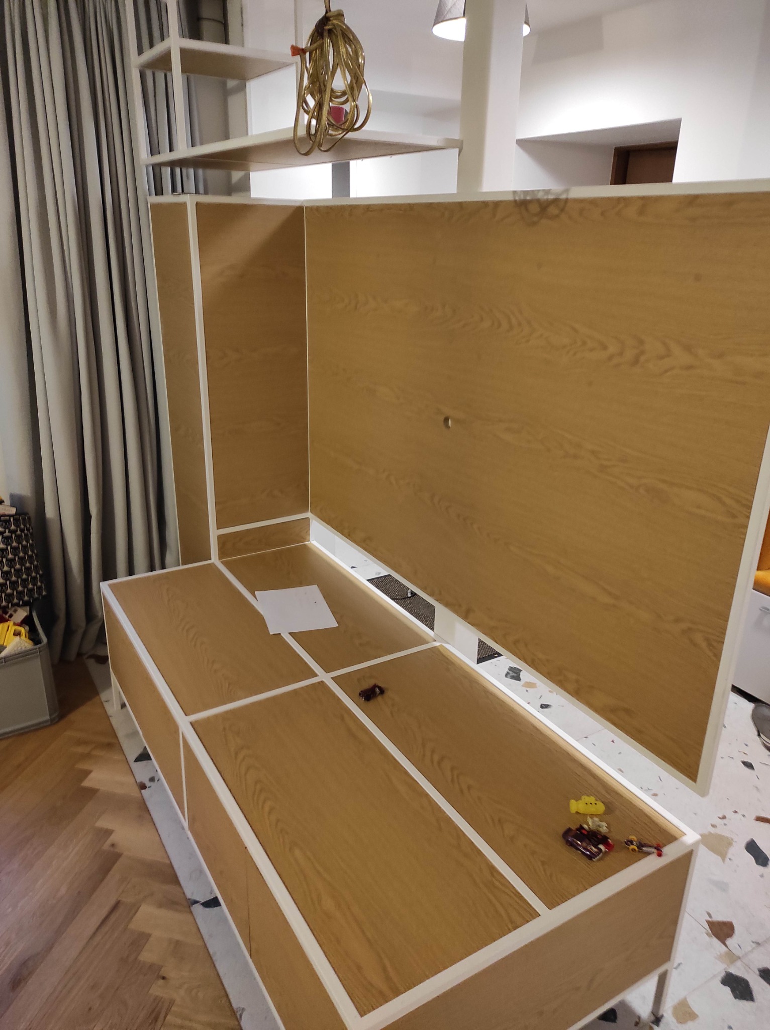 Montaż korpusu meblowego z drewnopodobną okleiną w Radomiu, widoczne zabawki na blacie i kartka papieru, sugerujące etap prac wykończeniowych.