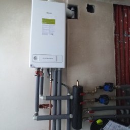 Usługi Hydrauliczne - Zamontowany, biały piec gazowy Beretta Mynute Green z orurowaniem, widoczne pompy obiegowe, instalacja w surowym stanie, ściany w trakcie wykańczania.
