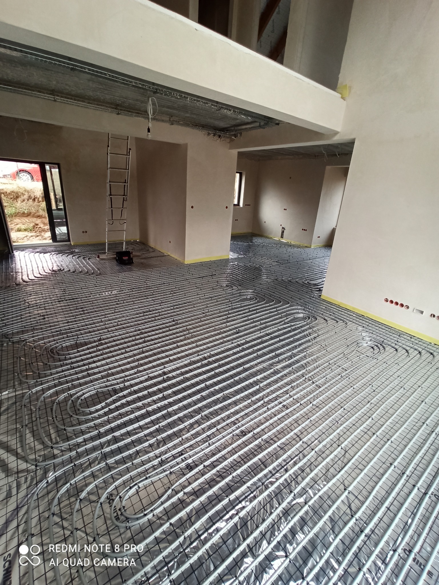 Rozłożona instalacja ogrzewania podłogowego na folii izolacyjnej w trakcie montażu w nowym domu w Olsztynie, widoczna drabina i przygotowane otwory na gniazdka.