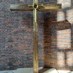 Metalowa konstrukcja krzyża z elementami dekoracyjnymi, zamontowana na tle ściany z cegły.