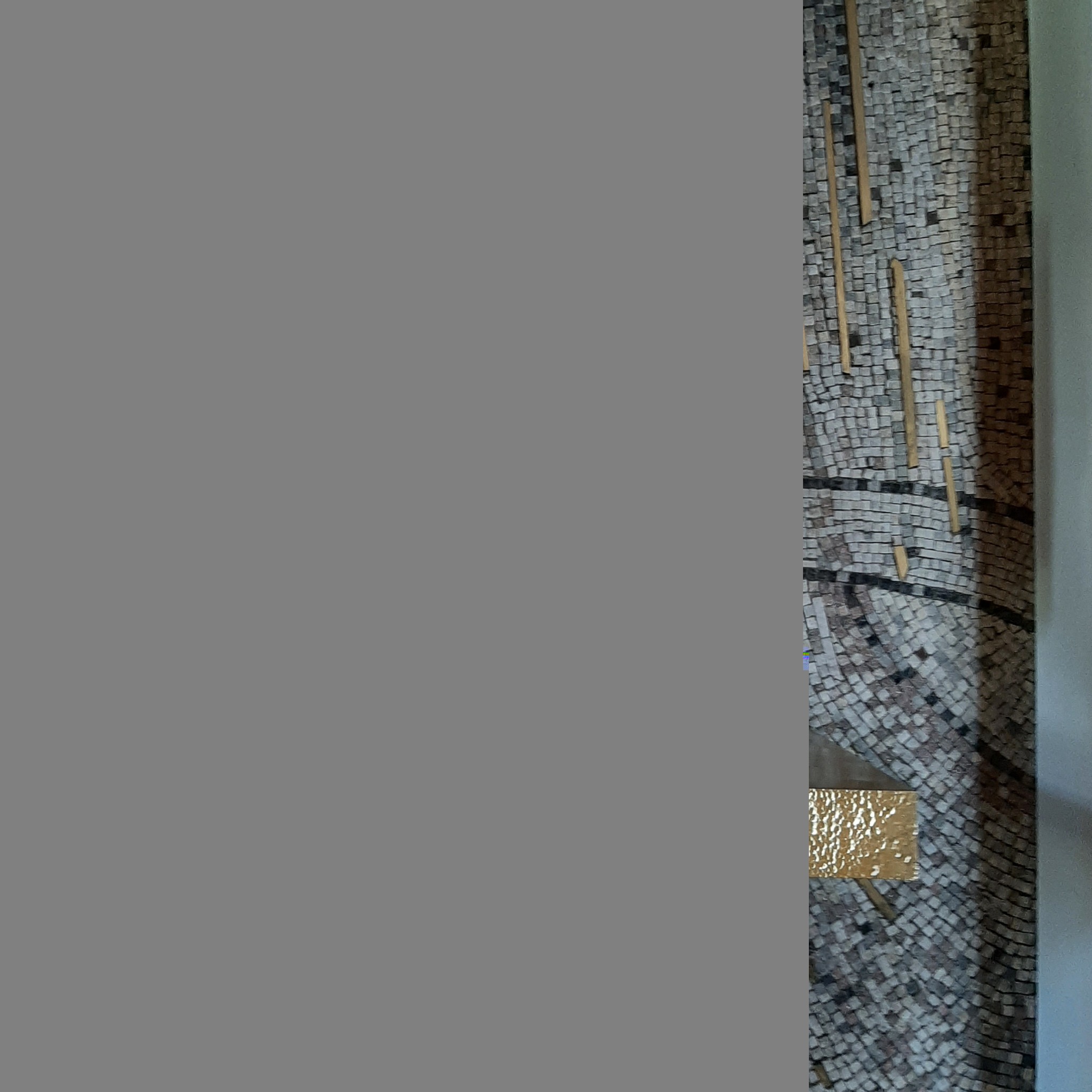 Mozaika ścienna z kamiennych kostek w odcieniach szarości i brązu, z wkomponowanymi elementami z jasnego drewna i jedną złotą kostką.