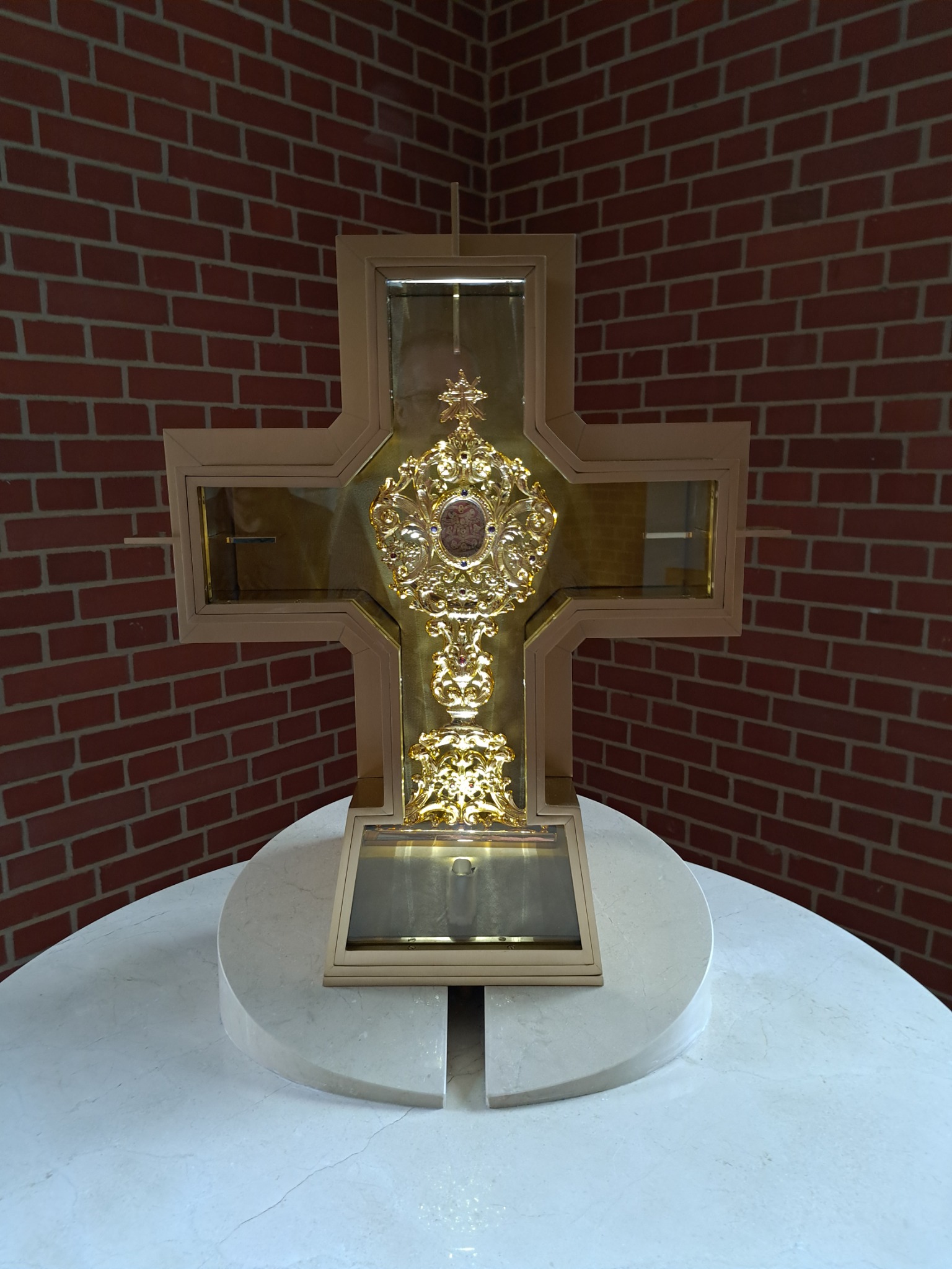 Krucyfiks z bogato zdobionym, złoconym relikwiarzem na marmurowym postumencie, tło z cegły