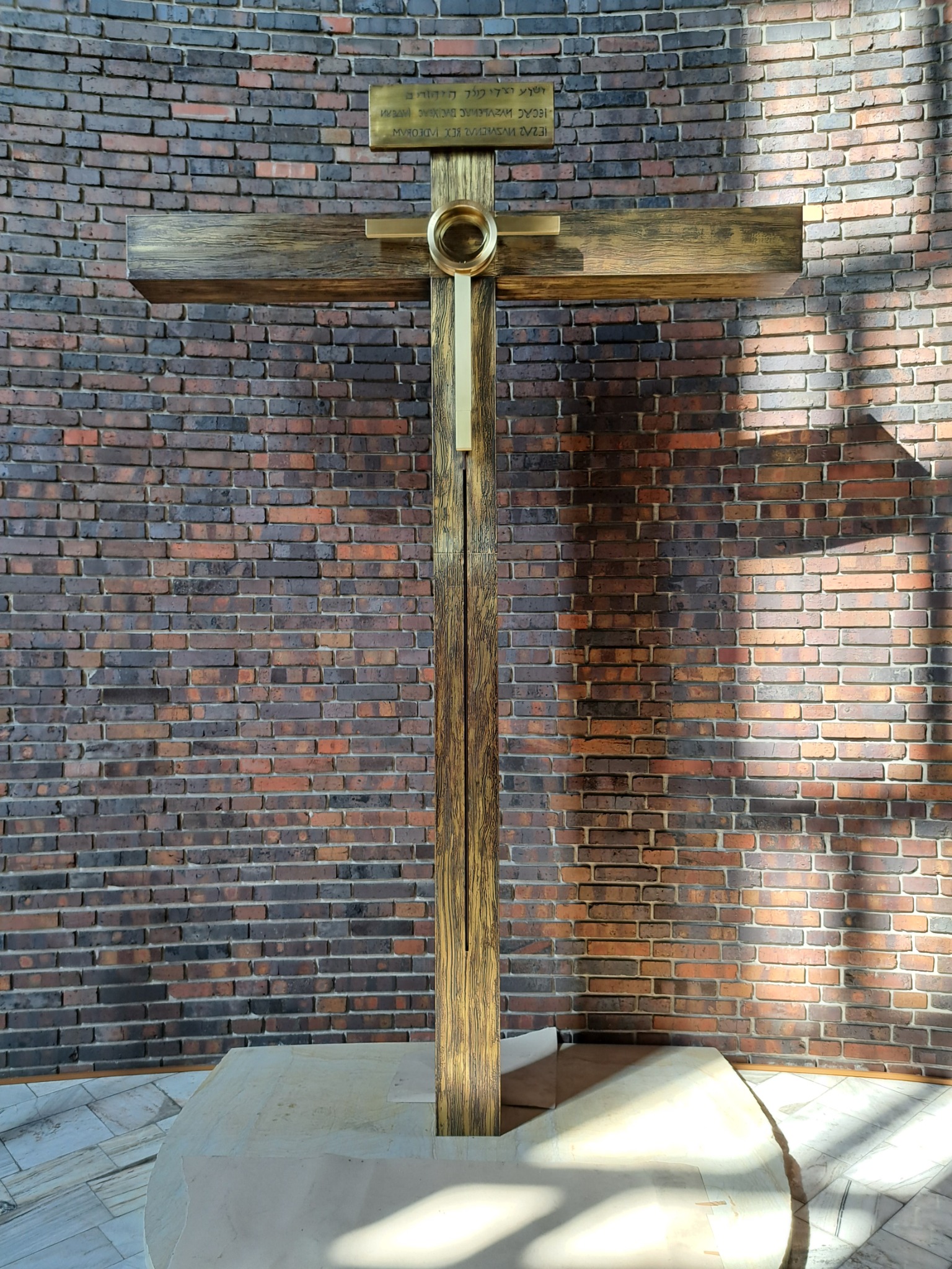 Metalowa konstrukcja krzyża z elementami dekoracyjnymi, zamontowana na tle ściany z cegły.