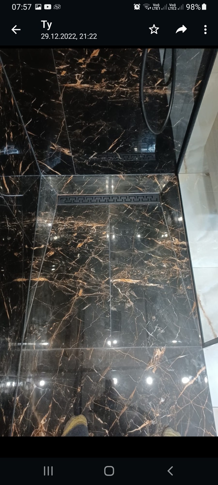 Wykończona kabina prysznicowa z czarnymi płytkami imitującymi marmur ze złotymi żyłami oraz odpływem liniowym z motywem greckim.