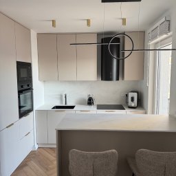 HouseOfDesign - Elegancka kuchnia w beżach i bieli. Nowoczesne oświetlenie, marmurowe blaty, drewniana podłoga w jodełkę. Minimalistyczny design z wyspą i hokerami.