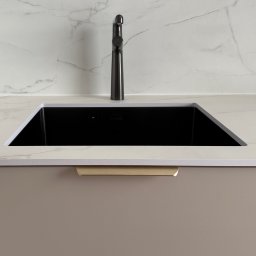 HouseOfDesign - Czarne, prostokątne zlewozmywak w blacie z marmurowym wzorem, z ciemną baterią i beżową szafką z uchwytem. Minimalistyczny design, neutralna kolorystyka.