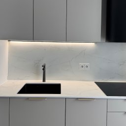 HouseOfDesign - Minimalistyczna kuchnia: szare szafki, czarny zlew i bateria, marmurowy blat z podświetleniem LED. Gniazdka elektryczne na ścianie.