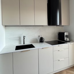 HouseOfDesign - Jasna kuchnia z czarnym zlewem i sprzętem SMEG. Minimalistyczny design z drewnianą podłogą w jodełkę i marmurowym panelem nad blatem.